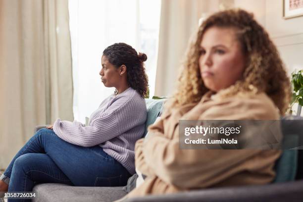 shot of an attractive young woman sitting on the sofa and ignoring her girlfriend after an argument - girlfriend stockfoto's en -beelden