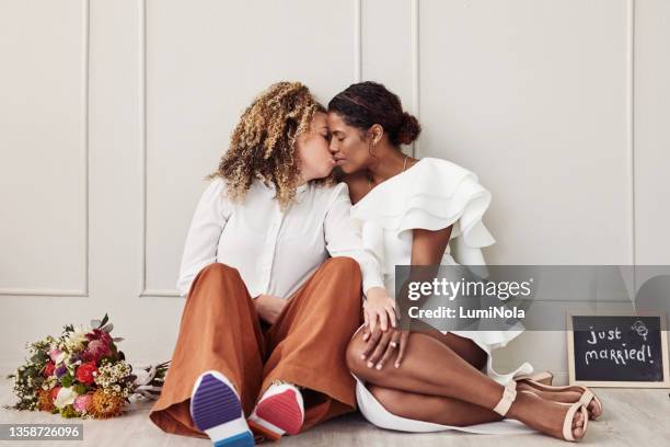 full length shot of a young lesbian couple sitting on the floor together and kissing after their wedding - lesbians kissing stock pictures, royalty-free photos & images