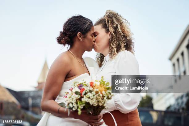 shot of a young lesbian couple standing outside together and kissing after their wedding - lesbians kissing stock pictures, royalty-free photos & images