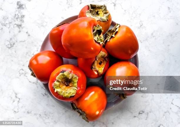 persimmons on a plate on white background - kaki stock-fotos und bilder