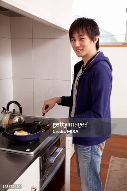 young man cooking sunny-side up egg - sunnyside eggs stock pictures, royalty-free photos & images
