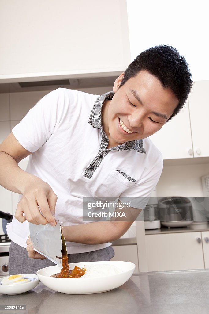 Young man pouring curry sauce from retort pouch to plate
