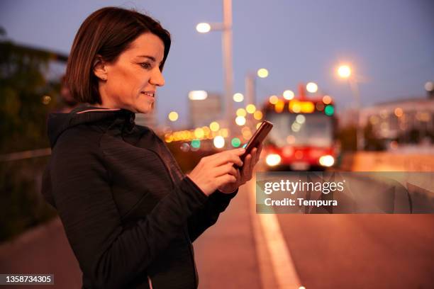 a woman is sending an sms at dusk in the city. - sportsperson stock pictures, royalty-free photos & images