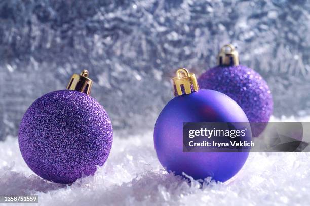 three christmas balls in trendy  color of the  year 2022 very peri purple violet  color on frozen window background. - three year stock pictures, royalty-free photos & images