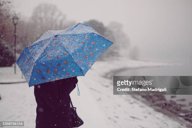 girl with heavy jogger in winter sheltering from snow and rain at night illuminated by lampposts with an umbrella - sleet stock pictures, royalty-free photos & images