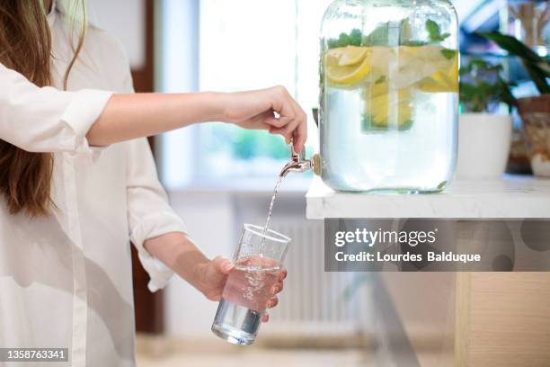 woman filling a glass of water from the fountain crystal - crystal glasses stockfoto's en -beelden