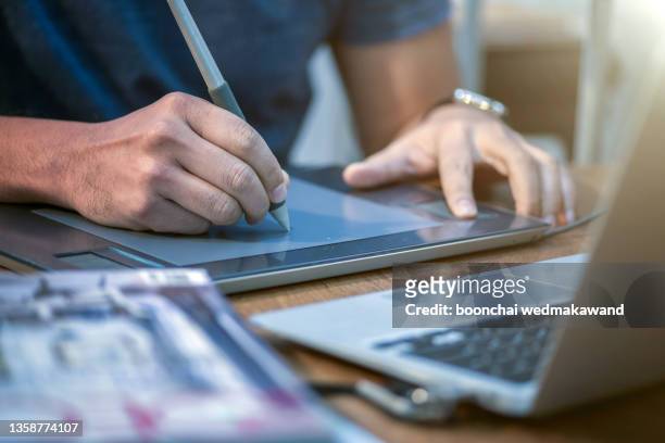 businessman in black suit working in modern office. business man with stylus pen signing on digital tablet screen, reviewing business report with laptop computer on glass table, close up - escritura no occidental fotografías e imágenes de stock