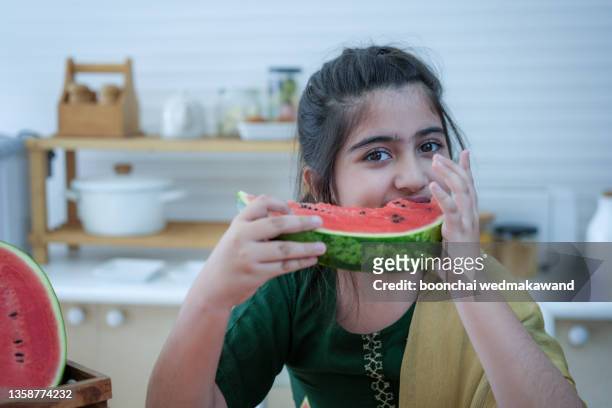 pretty indian/asian girl holding a slice of watermelon or tarbuja in hindi, standing isolated over white or yellow background. - child eating juicy stock pictures, royalty-free photos & images