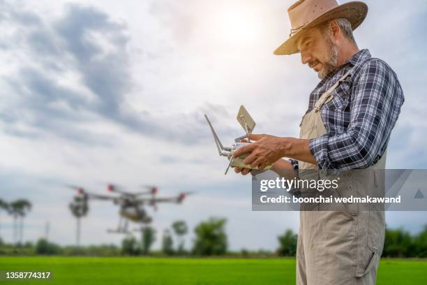 attractive farmer navigating drone above farmland with silos and tractor in background. high technology innovations for increasing productivity in agriculture - shifting cultivation stock pictures, royalty-free photos & images