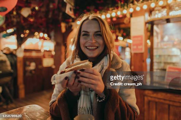 frau isst wurst und trinkt glühwein auf dem weihnachtsmarkt - christkindlmarkt stock-fotos und bilder