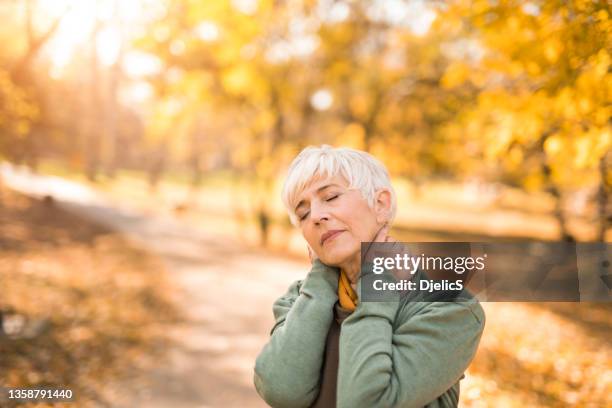 peaceful senior woman enjoying an autumn morning outdoors in nature. - neckache stock pictures, royalty-free photos & images