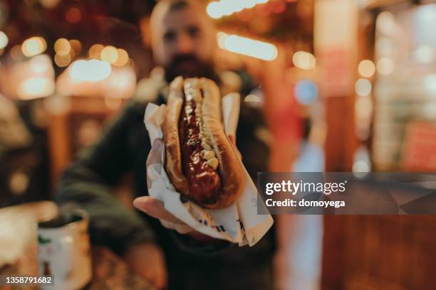 mann isst einen wurst hot dog und genießt einen weihnachtsmarkt - hot dog stock-fotos und bilder