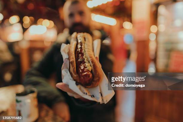 homem comendo um cachorro-quente salsicha e desfrutando de um mercado de natal - sausage - fotografias e filmes do acervo