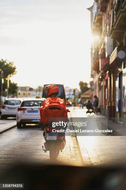 anonymous courier riding scooter on city street at sundown - cars on motor way stockfoto's en -beelden