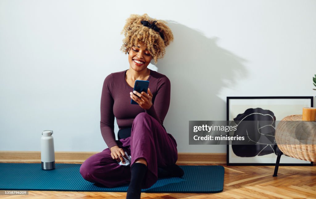 Mujer afroamericana tomando un descanso telefónico durante la práctica de yoga