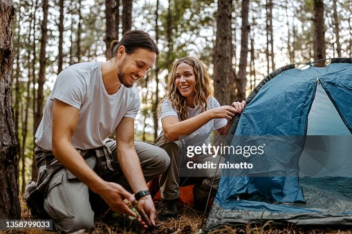 Pareja construyendo tienda de campaña en el bosque durante la caminata Pareja construyendo tienda de campaña en el bosque durante la caminata