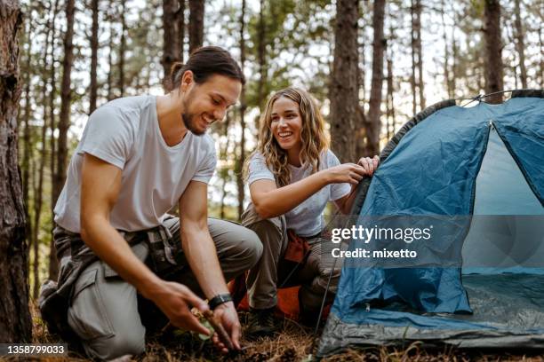 pareja construyendo tienda de campaña en el bosque durante la caminata - acampar fotografías e imágenes de stock