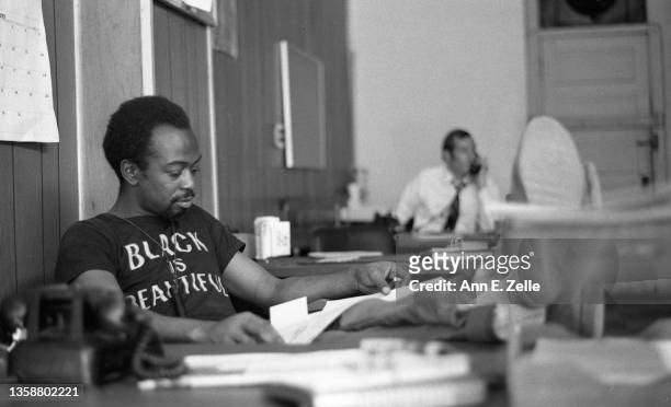 View of American artist and Art & Soul Director Jackie Hetherington as he sits at a desk, his feet up, in the Conservative Vice Lords office,...