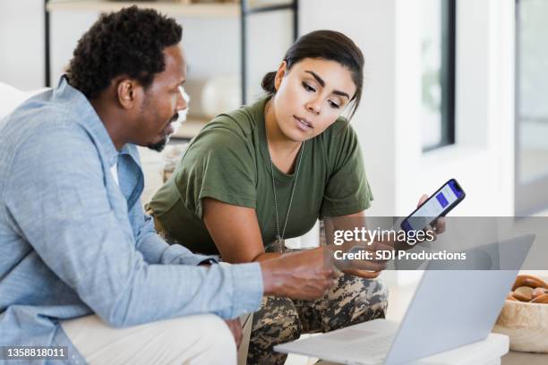 man and soldier wife discuss finances using phone and laptop - military wife stock pictures, royalty-free photos & images