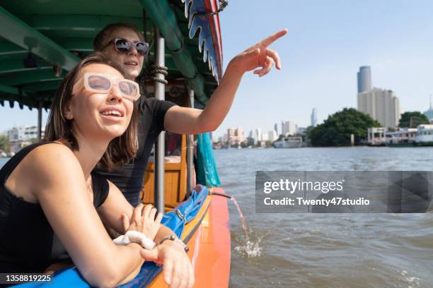 two caucasian women discover bangkok riding a boat in chao phraya river looking out from the boat - tour boat stock pictures, royalty-free photos & images