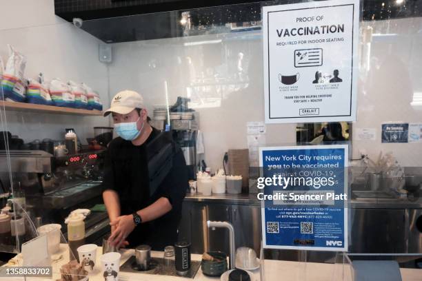 An employee at a coffee shop in Manhattan wears a masks as signs ask for proof of vaccination on the day that a mask mandate went into effect in New...