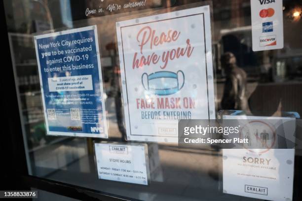 Sign on the door of a coffee shop in Manhattan ask for proof of vaccination and the wearing of a mask on the day that a mask mandate went into effect...