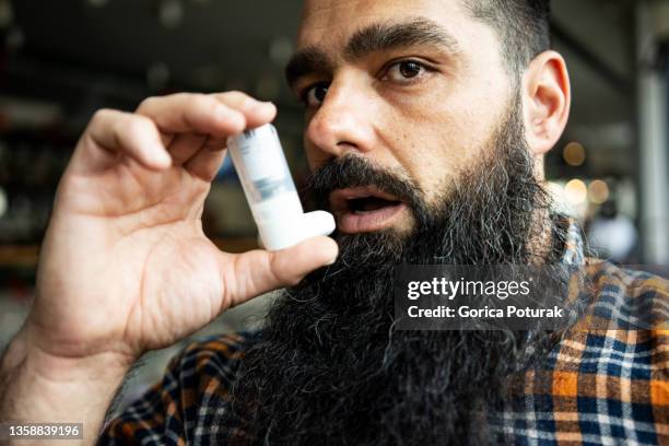 man using asthma inhaler, indoors - copd patient stockfoto's en -beelden