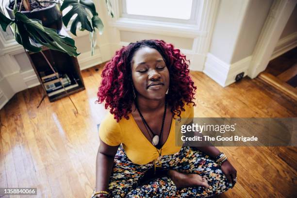 contented young woman sitting on floor meditating at home - woman sitting cross legged stock pictures, royalty-free photos & images