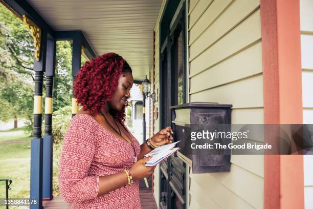 young woman in red dress checking mail on front porch - post imagens e fotografias de stock