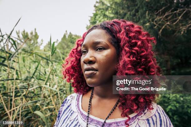 red curly haired young woman looking away from camera in woodland area - female looking away from camera serious thinking outside natural stock pictures, royalty-free photos & images