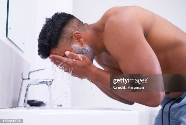 shot of a handsome young man rinsing off shaving cream from his face in the bathroom at home - man shaving face stock pictures, royalty-free photos & images