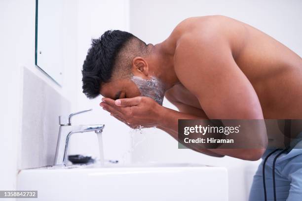 shot of a handsome young man rinsing off shaving cream from his face in the bathroom at home - man shaving foam stock pictures, royalty-free photos & images