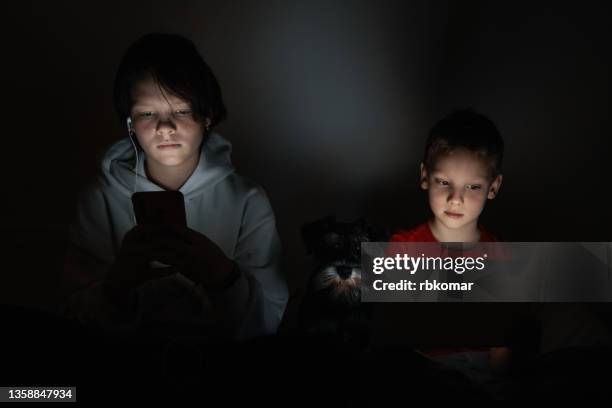 children sitting with a puppy in a dark room at night play with digital portable devices, tablets - children screen stock pictures, royalty-free photos & images