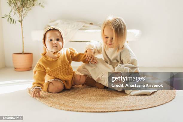 two little sisters are playing on a wicker carpet at cozy home. - small cotton plant stockfoto's en -beelden