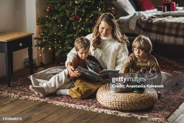 mother and sons siblings drinking cacao and reading book on cozy living room at home. - cosy christmas stock pictures, royalty-free photos & images