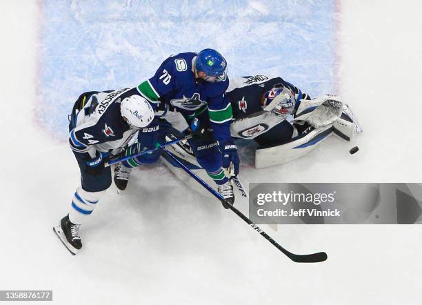 Tanner Pearson of the Vancouver Canucks and Josh Morrissey of the Winnipeg Jets look on as Eric Comrie of the Winnipeg Jets makes a save during their...