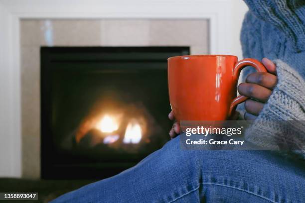 woman sits by fireplace with mug - hot older women fotografías e imágenes de stock