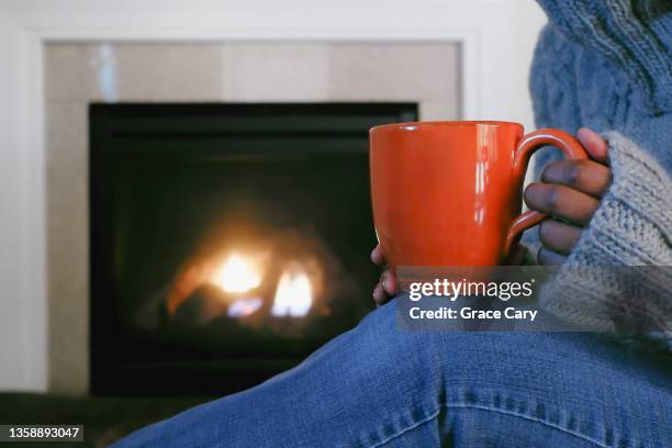 woman sits by fireplace with mug - mature woman winter stockfoto's en -beelden