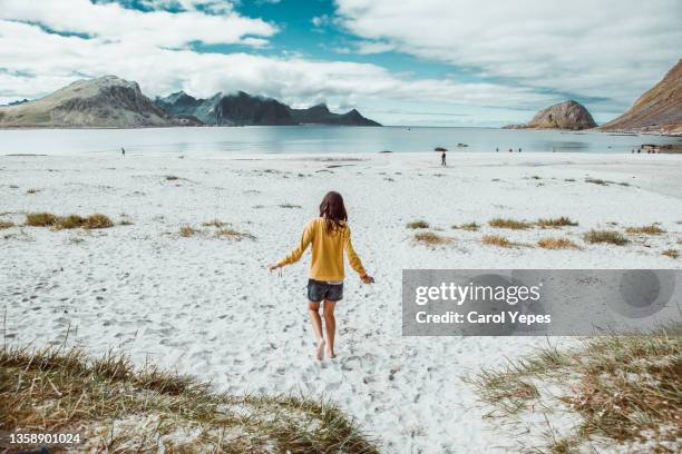 rear image of young woman walking alone in a remote beach in norway - traditionally norwegian stockfoto's en -beelden