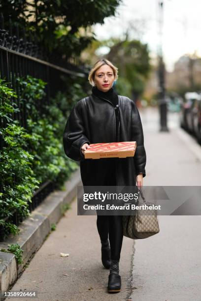 Emy Venturini wears a gold earrings, a black turtleneck pullover from Cos, a black shiny leather with black sheep interior oversized Vintage coat,...