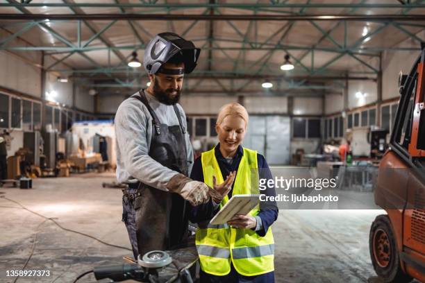 тwo factory workers in a big workshop talking over digital tablet. - steel worker stock pictures, royalty-free photos & images