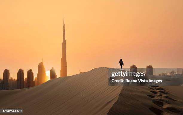 woman on a sand dune with futuristic city - dubai city stock-fotos und bilder