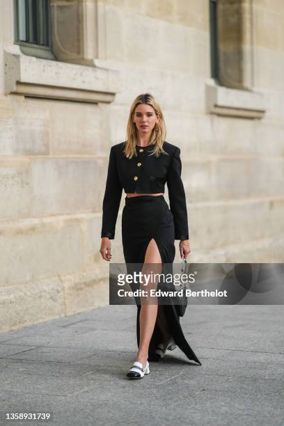 Natalia Verza wears a gold large Fendi earring, a black cropped jacket with gold large buttons, a high waits black slit / split long skirt, a gold...