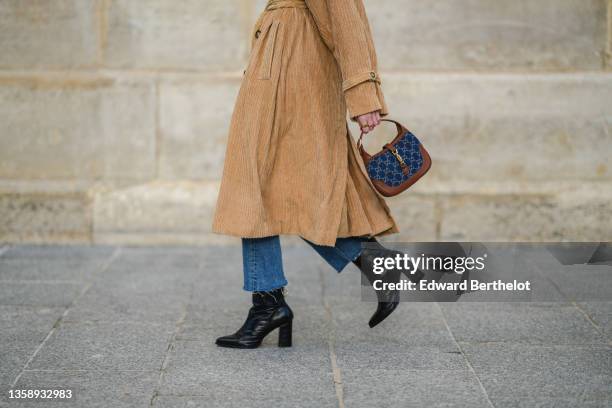 Alba Garavito Torre wears a beige ribbed velvet belted trench coat from Charlie Joe, blue denim ripped flared pants, gold rings, a blue denim GG...