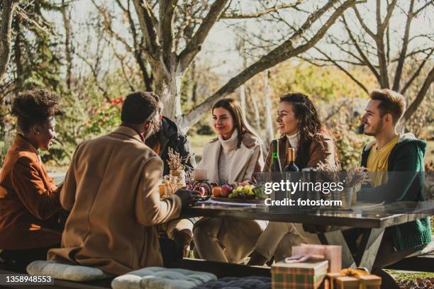 cheerful group of friends sitting at table outside, chatting and hanging out - house warming stock pictures, royalty-free photos & images