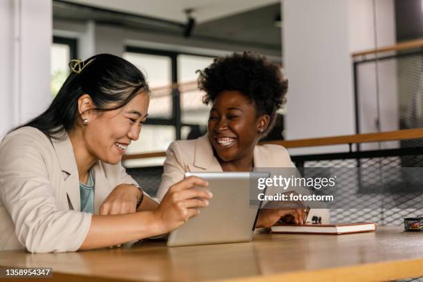 two businesswomen watching a funny video on digital tablet - asian young executive laughing office bildbanksfoton och bilder