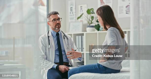 shot of a mature doctor sitting with his patient in the clinic and asking questions during a consultation - stomach stock pictures, royalty-free photos & images