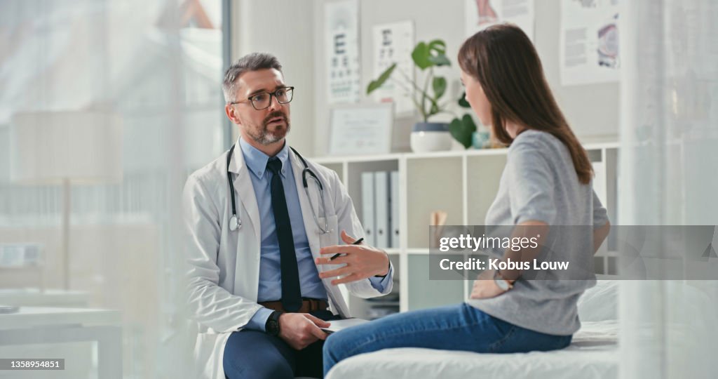 Shot of a mature doctor sitting with his patient in the clinic and asking questions during a consultation
