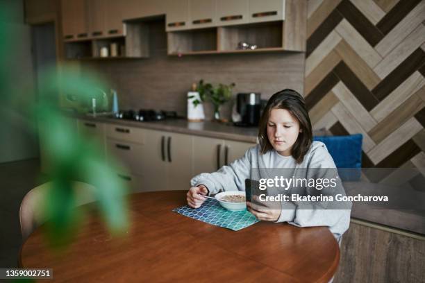 a 12-year-old girl with brown hair sits at home at the table and has breakfast muesli with milk - körperbewusstsein stock-fotos und bilder