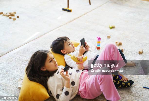 hermanos acostados en la alfombra y jugando, viendo dibujos animados en un teléfono inteligente - kids mess carpet fotografías e imágenes de stock